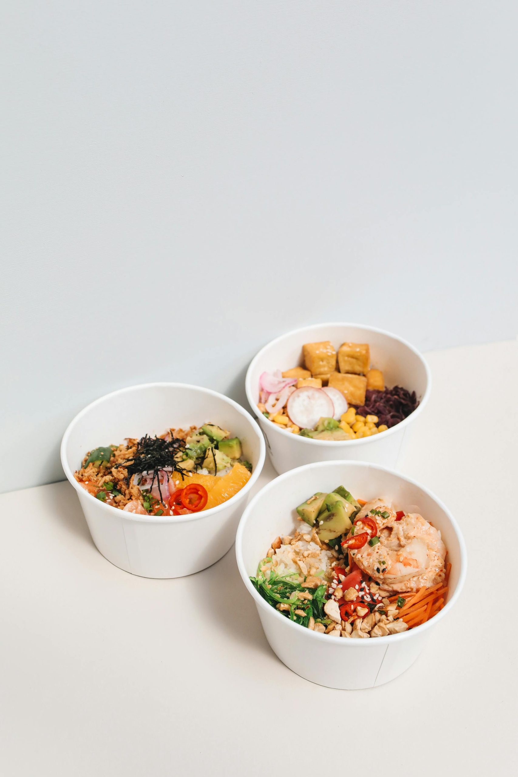 Three delicious healthy poke bowls with fresh ingredients on a white surface, perfect for food photography.